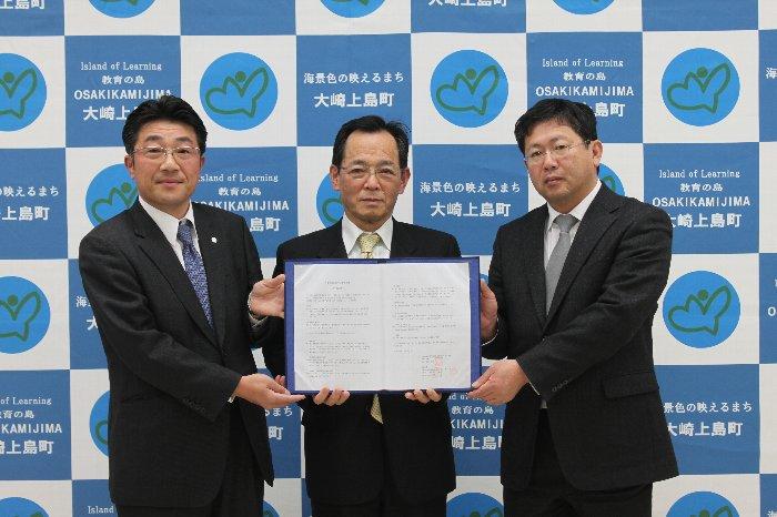 中央にいる大崎上島町長が胸の前に協定書を持ち、両脇の田中支店長、 豊田社長が協定書に両手を添えて3名で写っている写真