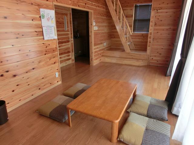 木材がふんだんに使われた床や壁で、机と座蒲団4枚が置かれている居間の写真